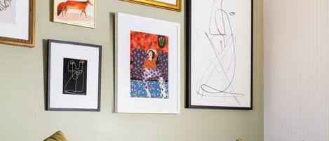 A living room with a checkered sofa, a glass coffee table, and various framed artworks on the wall.