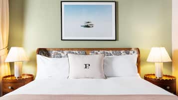 A neatly made bed with a pillow featuring a capital 'P', two bedside lamps, and a framed picture of a car on the wall.