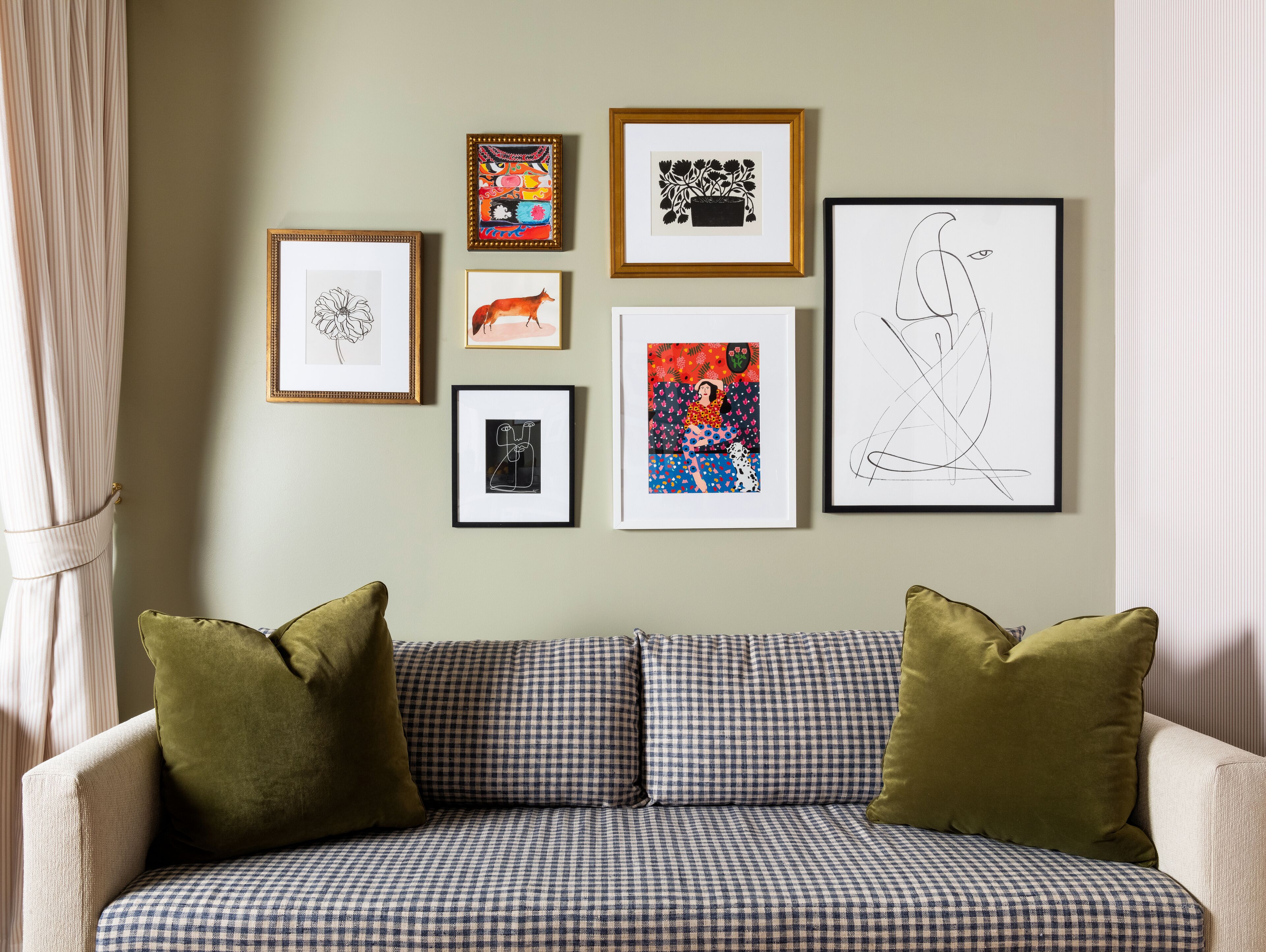 A living room with a checkered sofa, a green pillow, and six framed artworks on the wall.