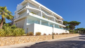 A modern two-story building with balconies, a stone wall, and tropical plants.