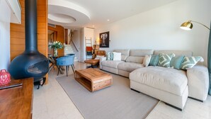 A modern living room with a black wood-burning stove, a beige sofa with patterned cushions, a wooden coffee table, and a floor lamp.