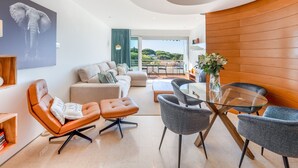 A modern living room with a sofa, armchairs, a glass coffee table, and a view of the outdoors.