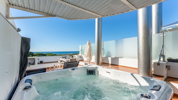 A hot tub on a rooftop deck with a clear view of the ocean.