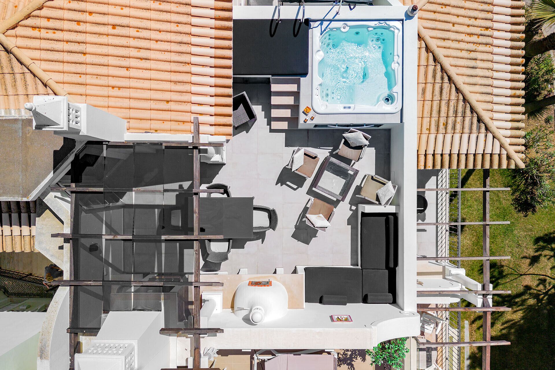 An aerial view of a rooftop with a hot tub, outdoor seating, and a staircase leading to an upper level.
