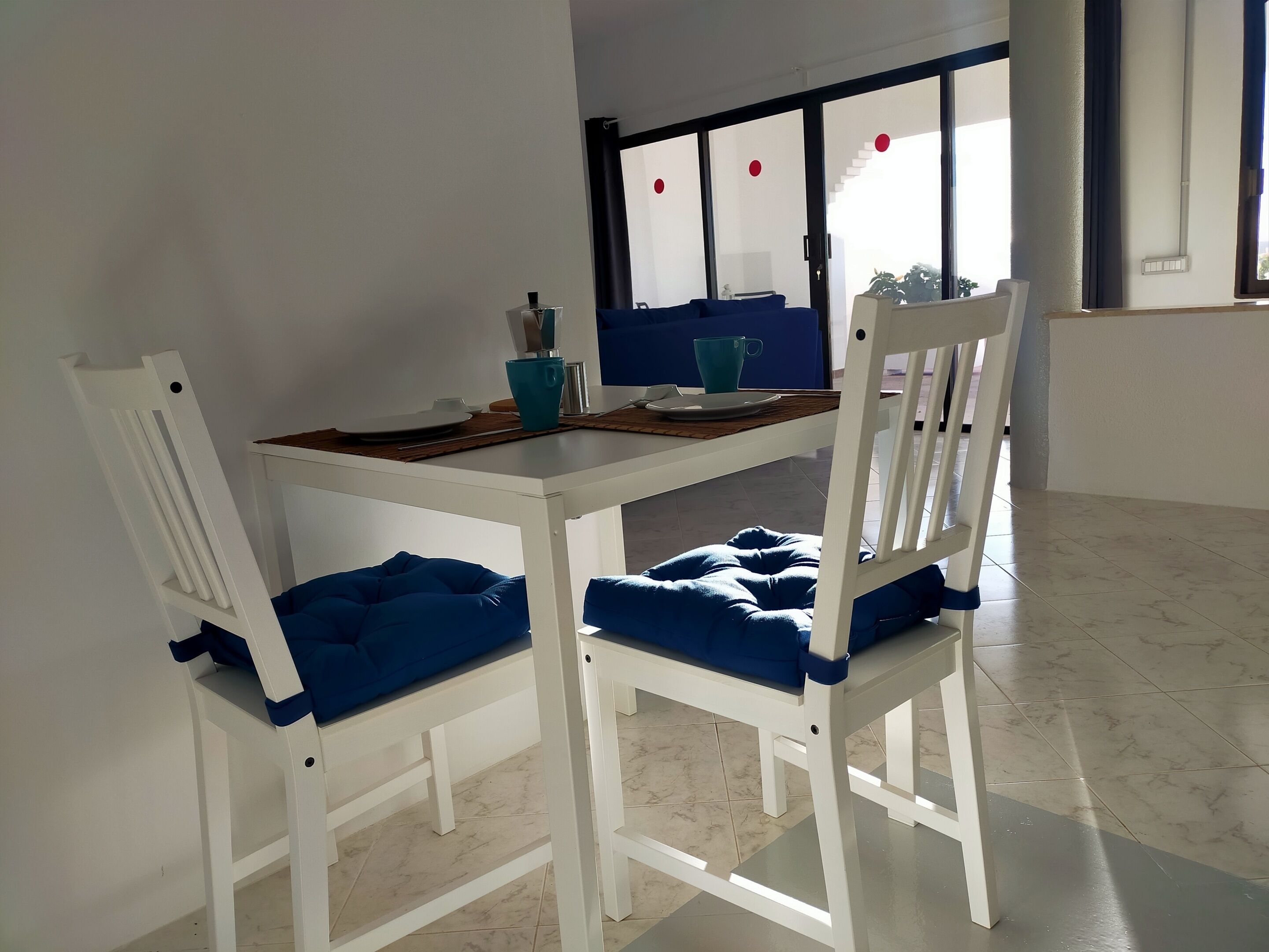 A white dining table with two chairs, each with a blue cushion.