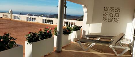 Une terrasse avec vue sur la mer, des rampes blanches et une table avec des chaises.