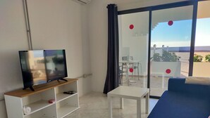 Een woonkamer met een televisie op een houten dressoir, een witte tafel en een blauwe bank.
