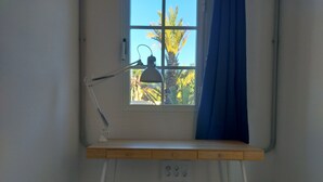 Een kamer met een bureau, een stoel, een raam met gordijn en een lamp.