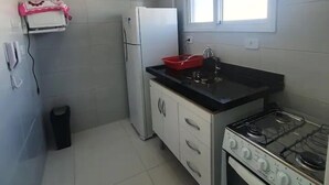 A small kitchen with white cabinets, a gas stove, a refrigerator, and a window. - Apto com vista pro Mar sacada gourmet (Praia Grande)