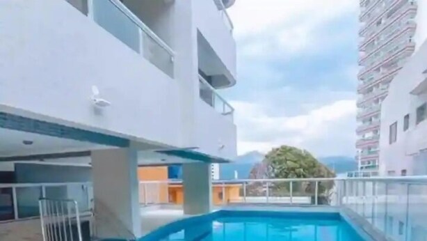 A swimming pool with a tiled deck, surrounded by a multi-story building with balconies. - Apto com vista pro Mar sacada gourmet (Praia Grande)