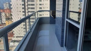 A balcony with a metal railing, a tiled floor, and a view of surrounding buildings. - Apto com vista pro Mar sacada gourmet (Praia Grande)