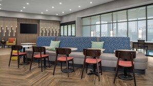 A modern lounge area with a sofa, chairs, and a TV screen. - Home2 Suites By Hilton Cullman (Cullman)