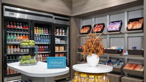 A hotel minibar with a variety of beverages and snacks, including a Hilton Honors sign. - Home2 Suites By Hilton Cullman (Cullman)