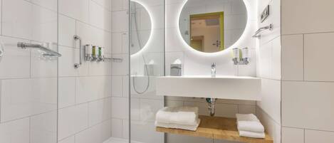 A modern bathroom with a glass-enclosed shower, a vanity with a mirror, and a wooden shelf with towels.