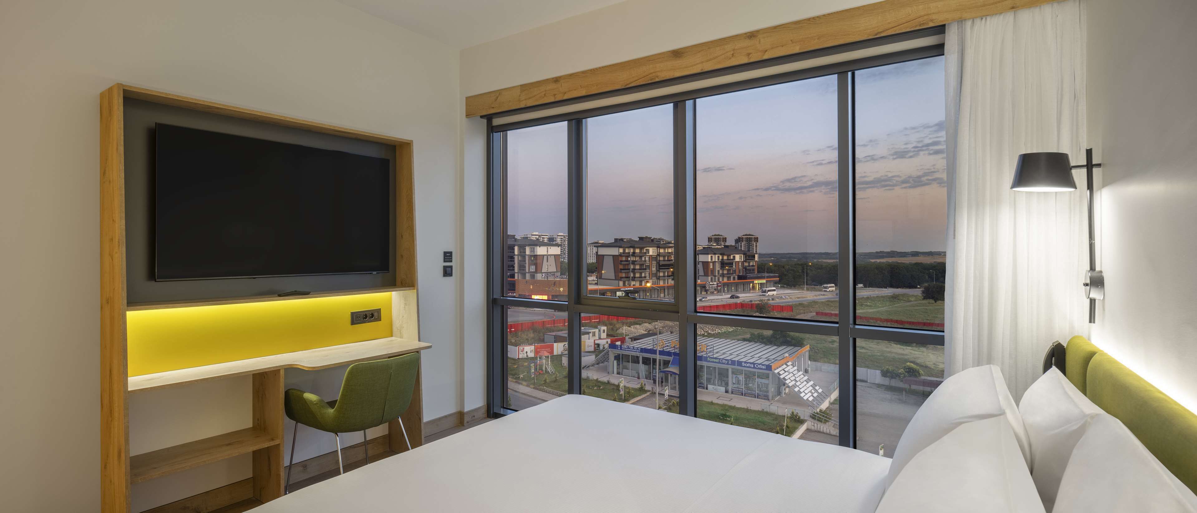 A hotel room with a large window, a flat-screen TV, a desk with a chair, and a bed.