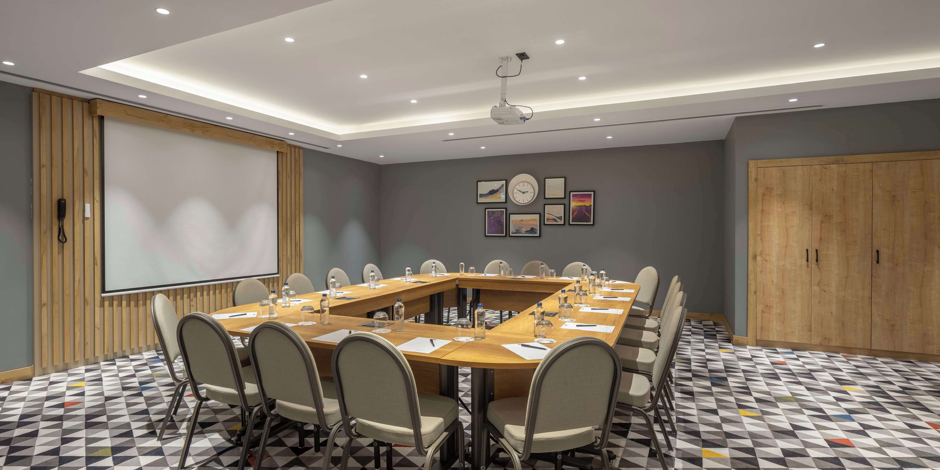 A conference room with a long table, chairs, a projector, and a screen.
