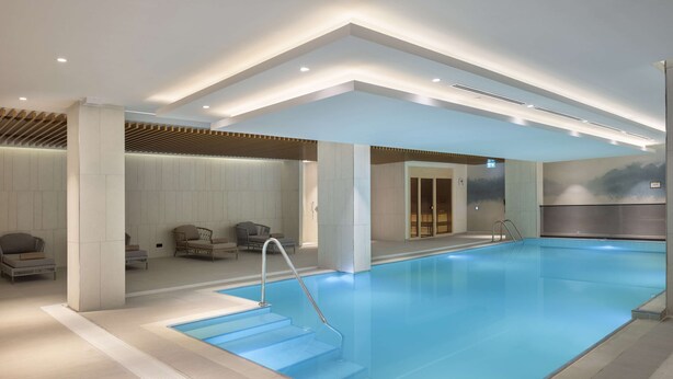 Una piscina interior amb disseny modern, amb aigua blava cristal·lina, un conjunt d'escales que hi condueixen i una zona de seients amb cadires i un sofà.
