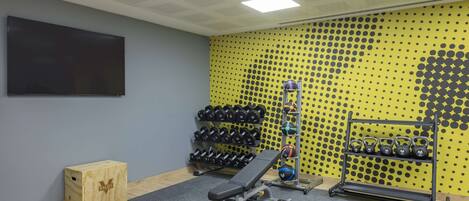A gym with a bench, dumbbells, kettlebells, and a yoga mat.