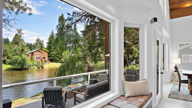 Eine Terrasse mit Blick auf ein Haus und einen Fluss, ausgestattet mit einem Tisch, Stühlen und einer Bank.