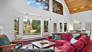 Ein geräumiges Wohnzimmer mit einem großen, roten Sofa, einem Holztisch und Blick auf ein Haus durch große Fenster.