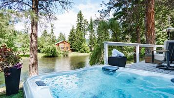 A hot tub on a deck with a view of a lake and a cabin in the background.