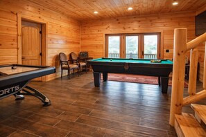 A pool table in a wooden cabin with a door and windows.