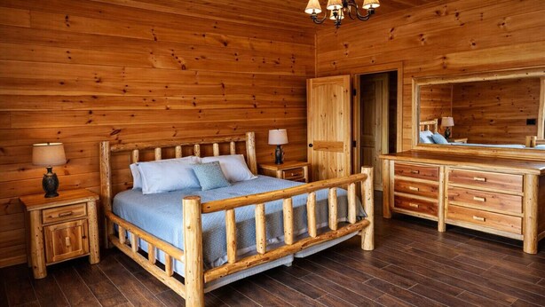 Une chambre dans une cabane en bois, avec un lit, des tables de chevet, une commode et un miroir.