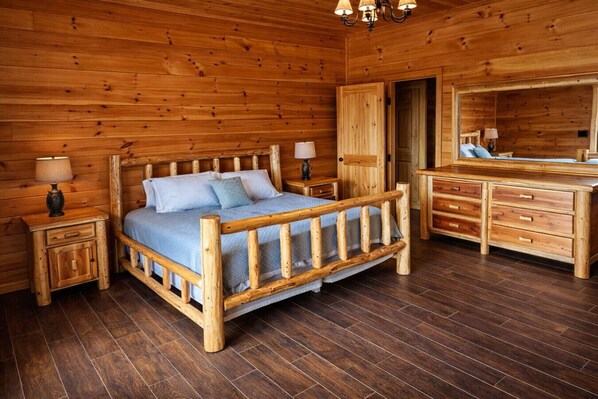 A wooden cabin bedroom with a bed, nightstands, a dresser, and a mirror.