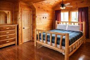 A wooden cabin room with a bed, dresser, and a ceiling fan.
