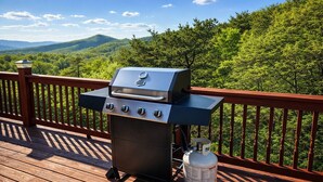 Un barbecue installé sur une terrasse en bois, offrant une vue magnifique sur des collines verdoyantes.