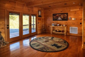 A wooden cabin interior with a large wooden door, a rug, a framed picture, and a small table with items on it.