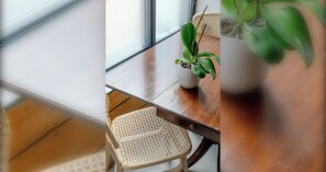 Ein Zimmer mit einem Holztisch, einem Korbstuhl und einer Topfpflanze.