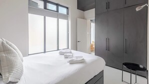 Un dormitorio con cama, ropa de cama blanca, un ventanal grande y un armario.