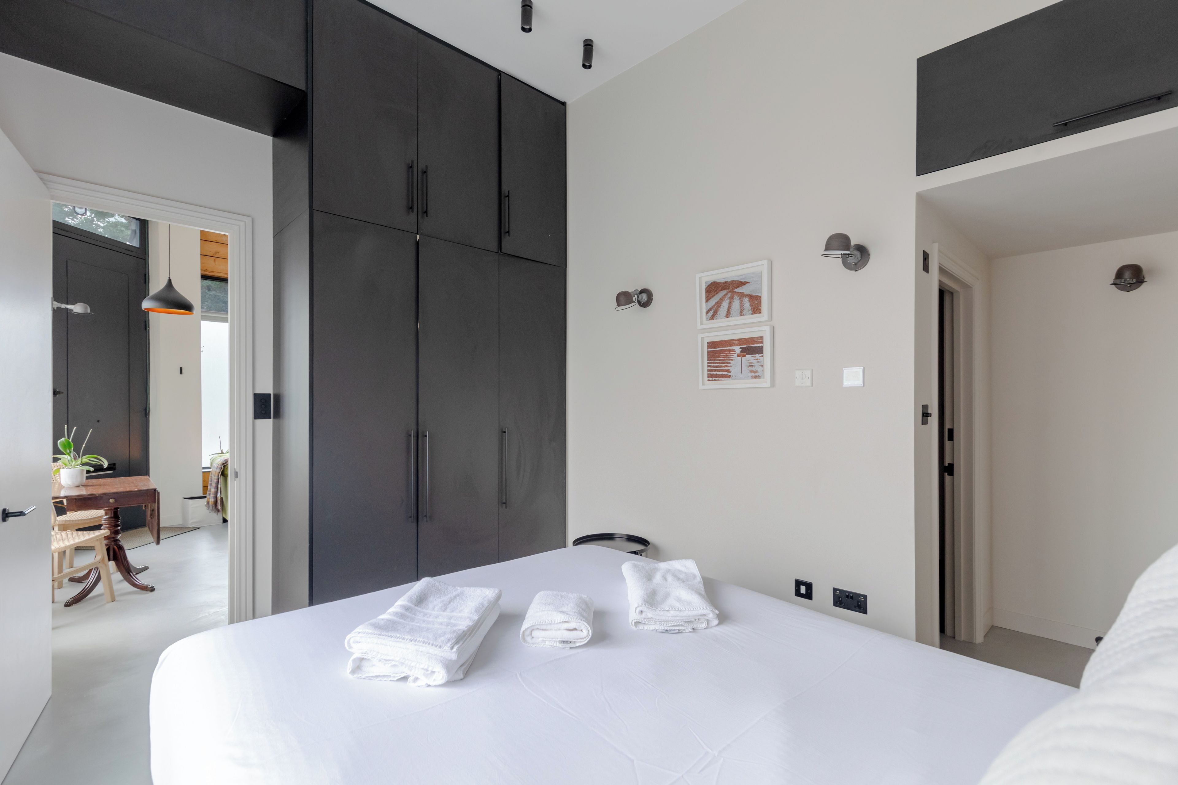 A modern bedroom with a large bed, dark wardrobe, and a small desk with a chair.
