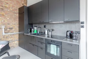 A modern kitchen with grey cabinets, a stainless steel countertop, a built-in oven, and a brick wall. - Stylishly Designed 1BDR Flat by Battersea Park (London)