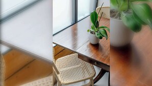 Una habitación con una mesa de madera, sillas de mimbre, una planta en maceta y una ventana.