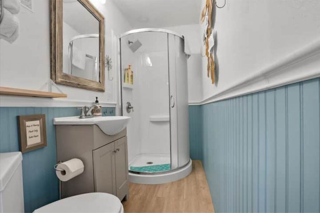A bathroom with a shower, toilet, sink, and mirror.