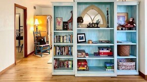 Une pièce avec un plancher en bois, une bibliothèque remplie de livres et d’objets décoratifs, une lampe et une chaise.