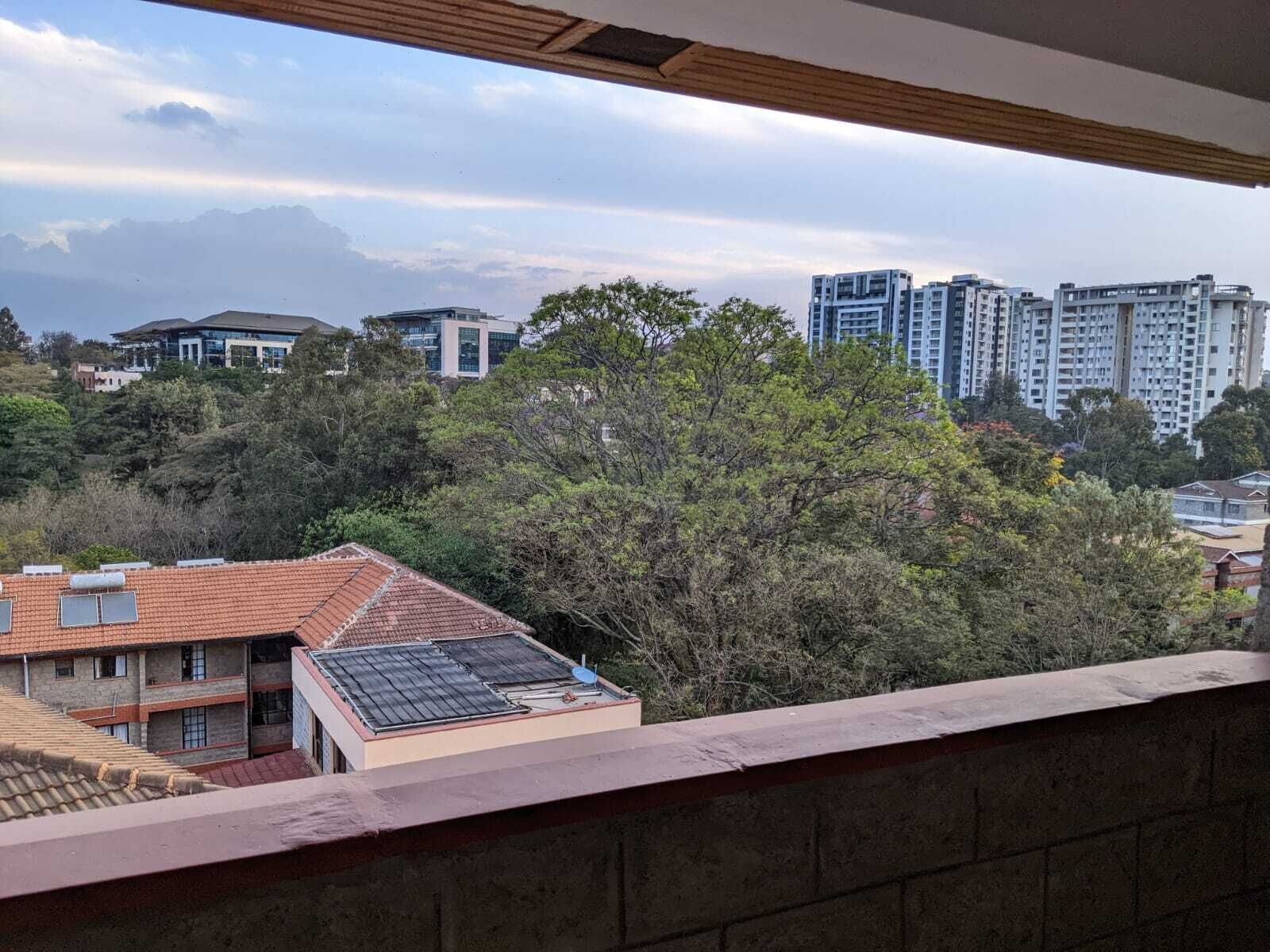 A view from a balcony overlooking a residential area with trees and modern buildings.