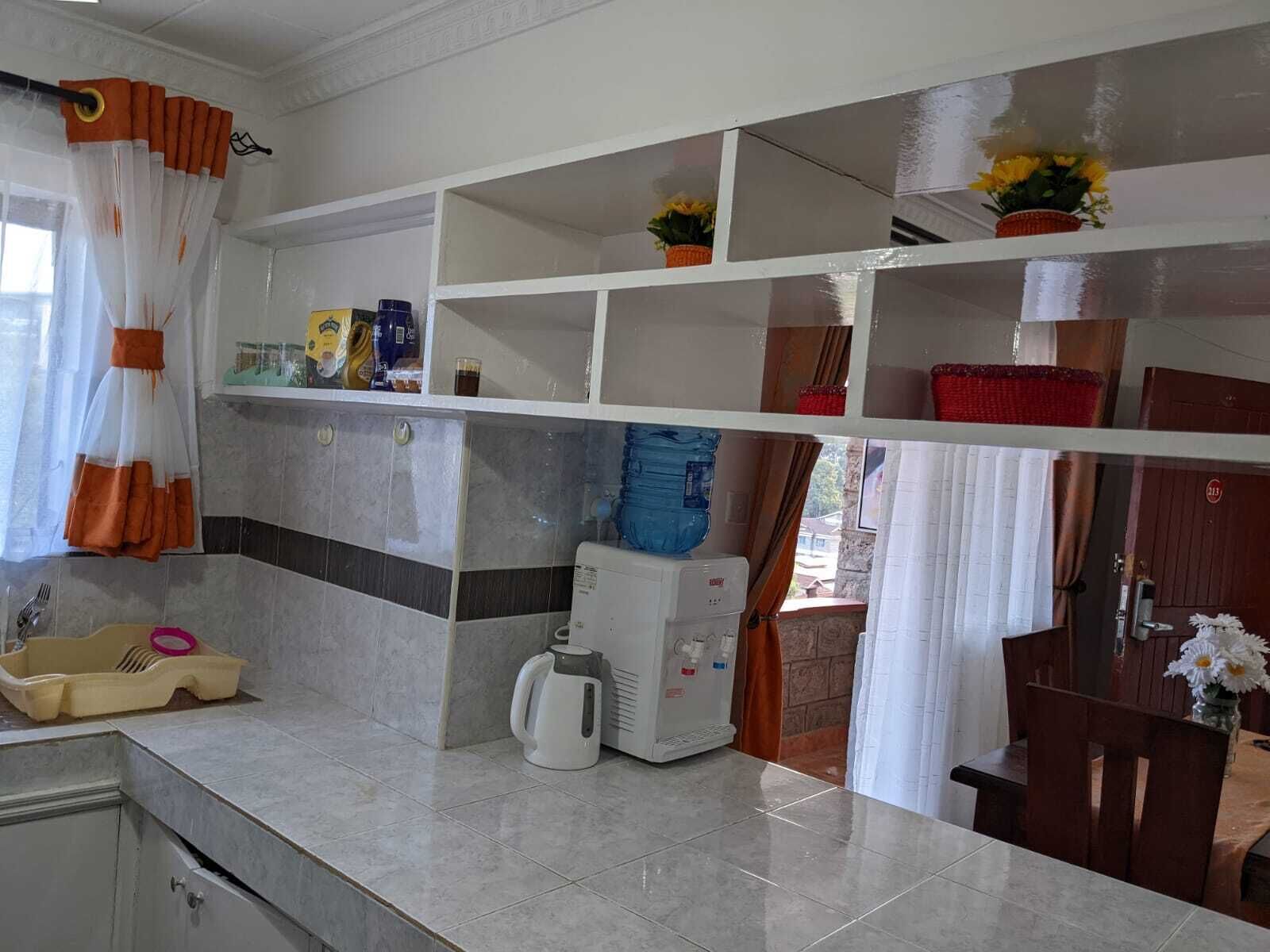 Una cocina con cafetera, un lavabo y varios utensilios de cocina en estantes.