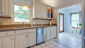 Cucina con mobili bianchi, lavastoviglie in acciaio inossidabile e una finestra che offre luce naturale.
