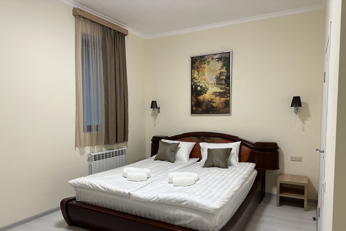 Una cama bien tendida con sábanas blancas y dos almohadas, un cabecero de madera, un cuadro en la pared y una mesita de noche.