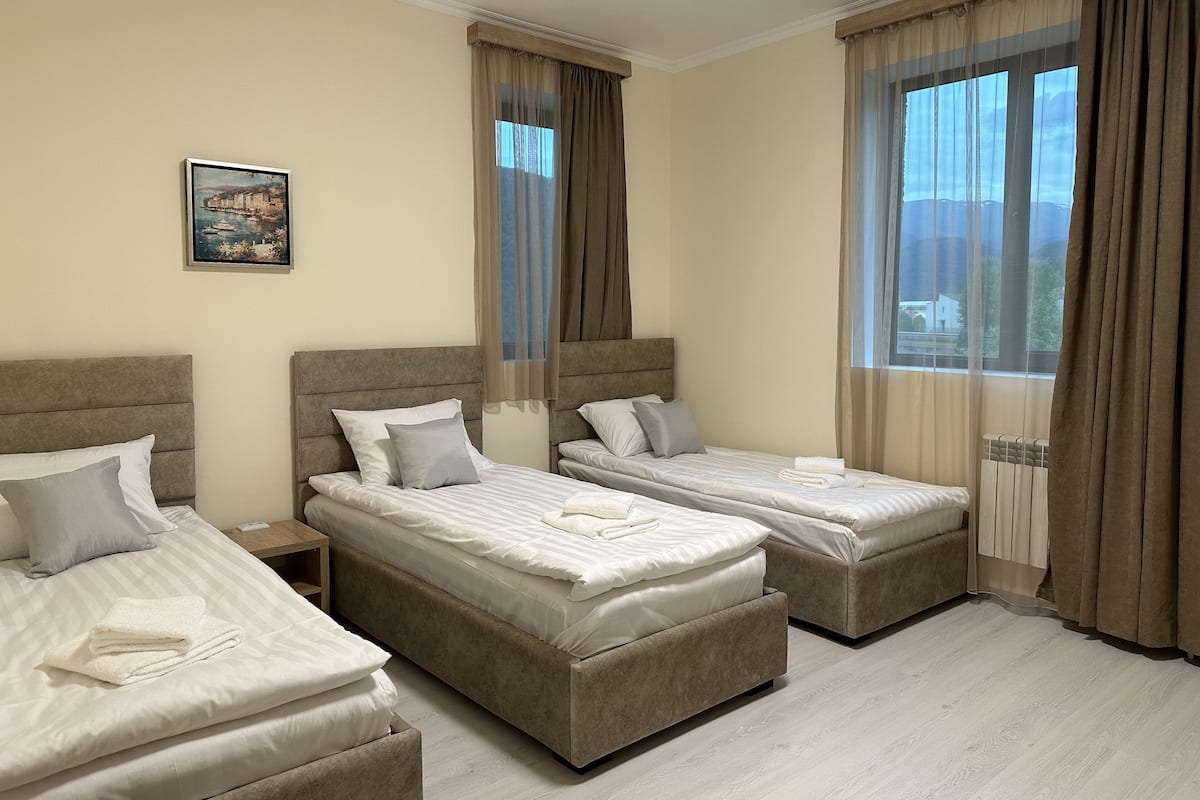 Habitación de hotel con dos camas, una mesita de noche, un cuadro y ventanas amplias con cortinas.