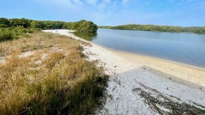 A sandy beach with a calm lake and a forested island in the distance. - Fenimore Mill 10E - Pool, Hot Tub, Boat Parking! (Cedar Key)