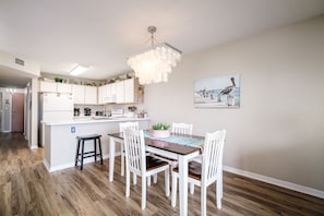 A modern kitchen with white cabinets, a central island, and a dining area with white chairs.