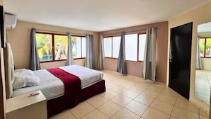 A spacious hotel room with a large bed, multiple windows, and a sliding door. - Quinta del Carmen (La Libertad)