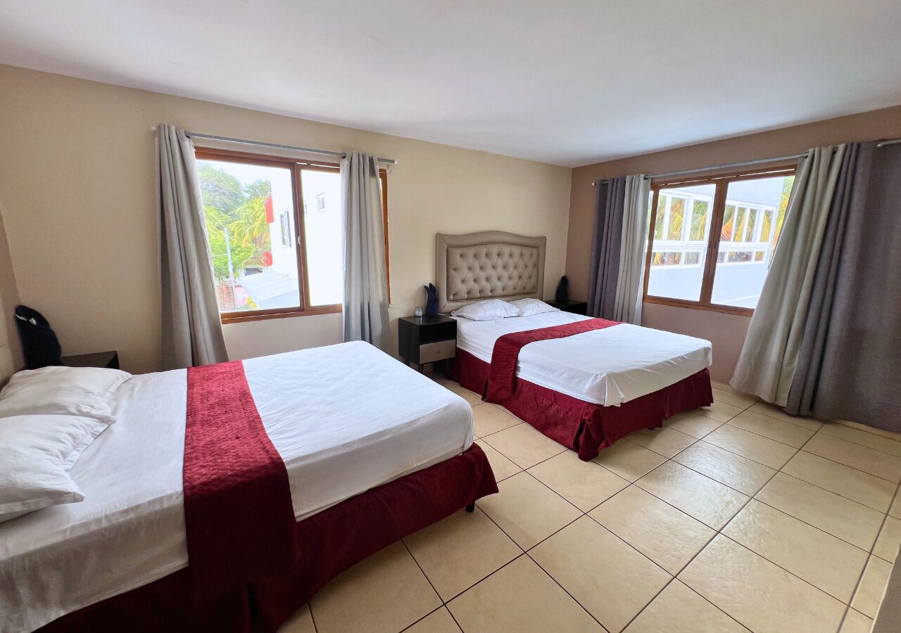 A hotel room with two beds, each with a red bedspread and white linens, a nightstand, and a window with curtains.