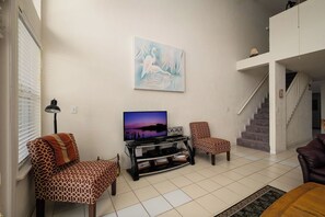 Ein Wohnzimmer mit Flachbildfernseher, gemusterten Sofas, einer Treppe und einem Bild an der Wand.