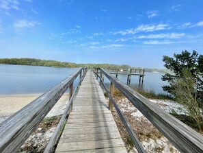 A wooden pier extending into a calm lake with a sandy beach at the end. - Fenimore Mill 2F - Gulf Front, Pool, Pet Friendly! (Cedar Key)