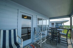 A covered porch with a table and chairs, a striped chair, and a view of a house in the background. - Fenimore Mill 2F - Gulf Front, Pool, Pet Friendly! (Cedar Key)